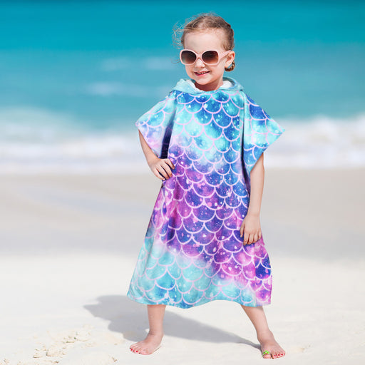 Child wearing mermaid scale hooded poncho towel in turquoise purple gradient on sandy beach